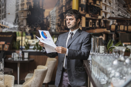 Бизнесмен стоит у барной стойки и внимательно изучает документы