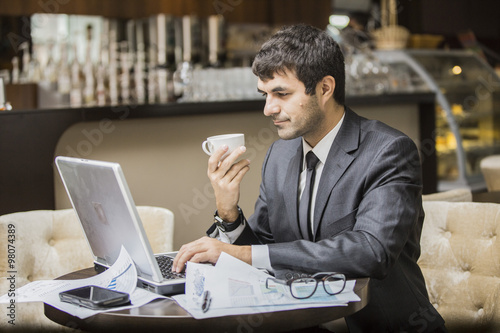 Молодой бизнесмен в кафе увлеченно читает новости в ноутбуке и радуется