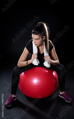 power fitness girl sitting on red fitness ball isolated on black