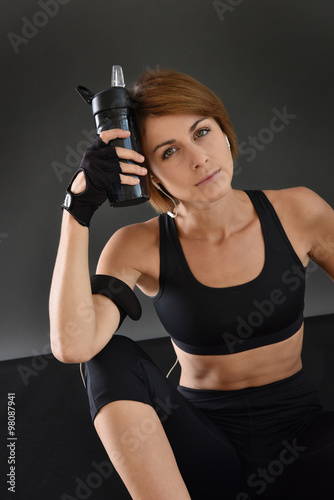 Fitness girl sitting on gym floor and holding bottle, isolated © goodluz