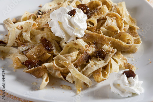 Crepes cut into strips with a filling of honey, minced walnuts and almonds, raisins and whipped cream, served on a white plate. 