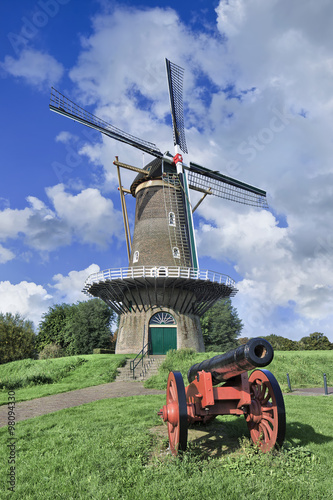 Ancient round brick floor mill on a city wall with a red canon and blue sky.