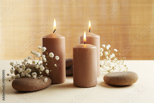 Beautiful composition of alight candles with pebbles and flowers on the table