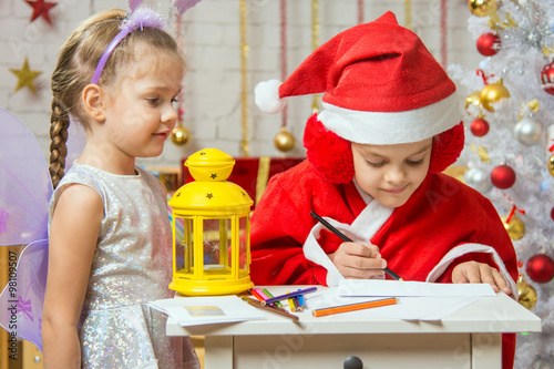 Girl dressed as Santa Claus signs the envelope with a letter, standing next to a girl dressed as fairies
