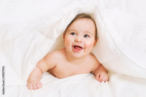 Happy Baby lies on bed under the blanket
