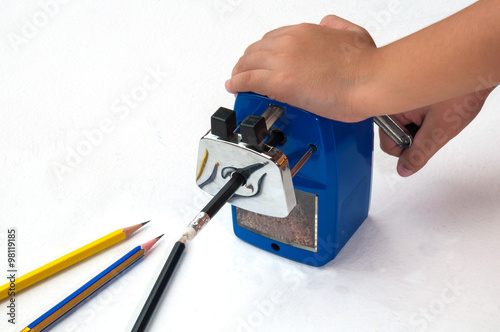 Cuadro en lienzo A boy is sharpening his pencil using mechanical sharpener over white background