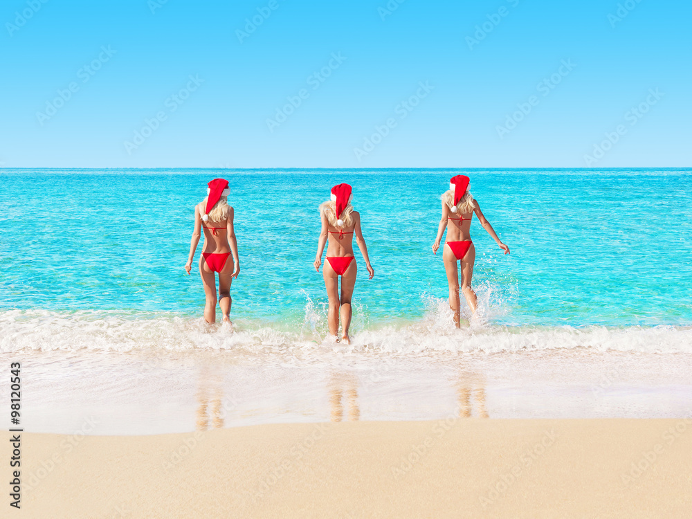 Women in christmas hats on ocean beach running to waves