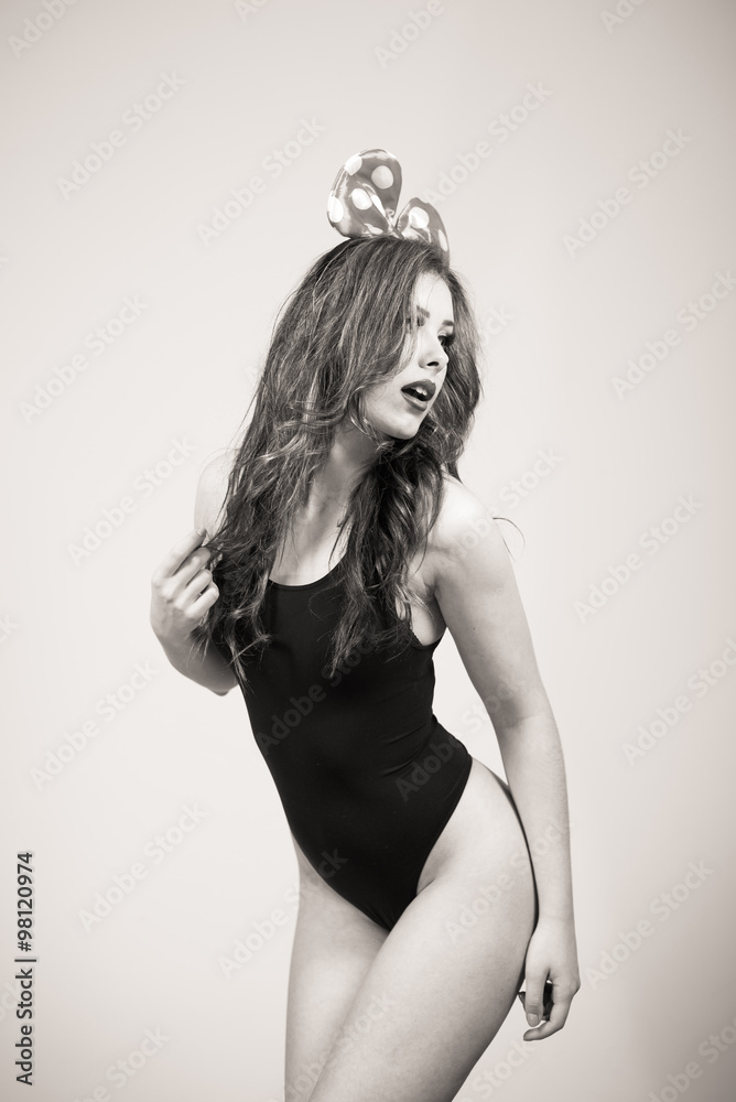 Fototapeta premium Black and white portrait of sexy beautiful young lady having fun wearing bunny ears posing on light copy space background
