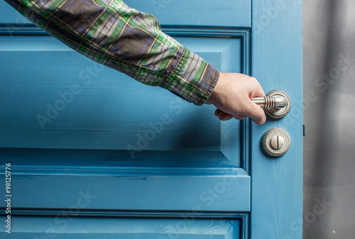 man holding on to by its metal handle in the open wooden door blue