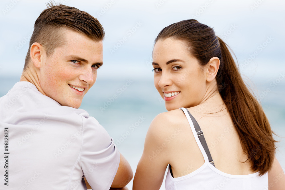 Young couple looking at camera while sitting next to each other on beach Young couple looking at camera while sitting next to each other on beach