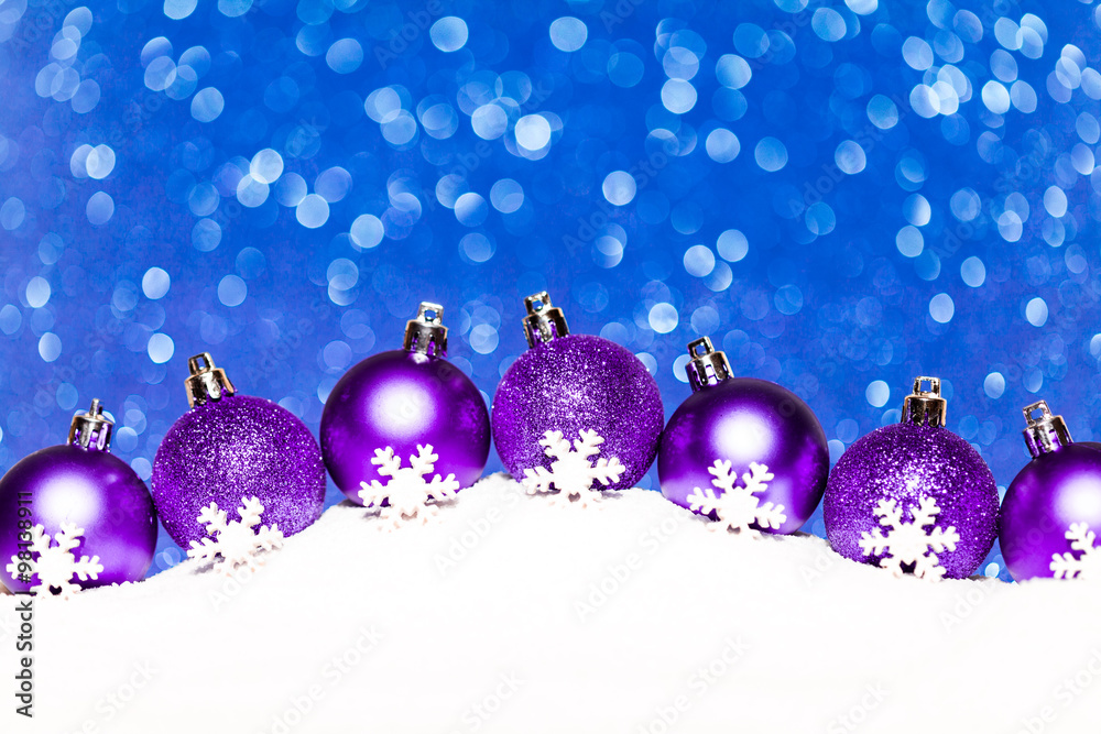 christmas purple balls in snow on blue glitter background christmas purple balls in snow on blue glitter background