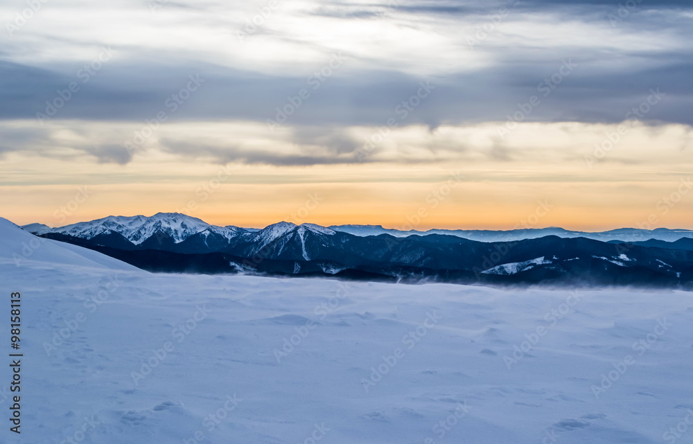 Evening winter landscape snowy peaks. Snow dust. Dusk. Orange sky, purple clouds and snow. True colors.