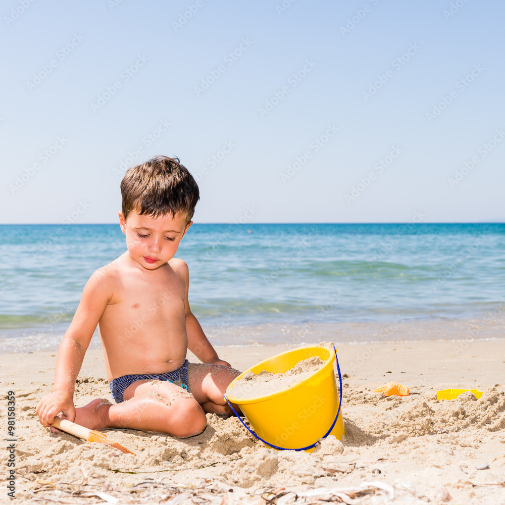 cute caucasian child playing on the beach with pail and shovel in a sunny day with sea background cute caucasian child playing on the beach with pail and shovel in a sunny day with sea background