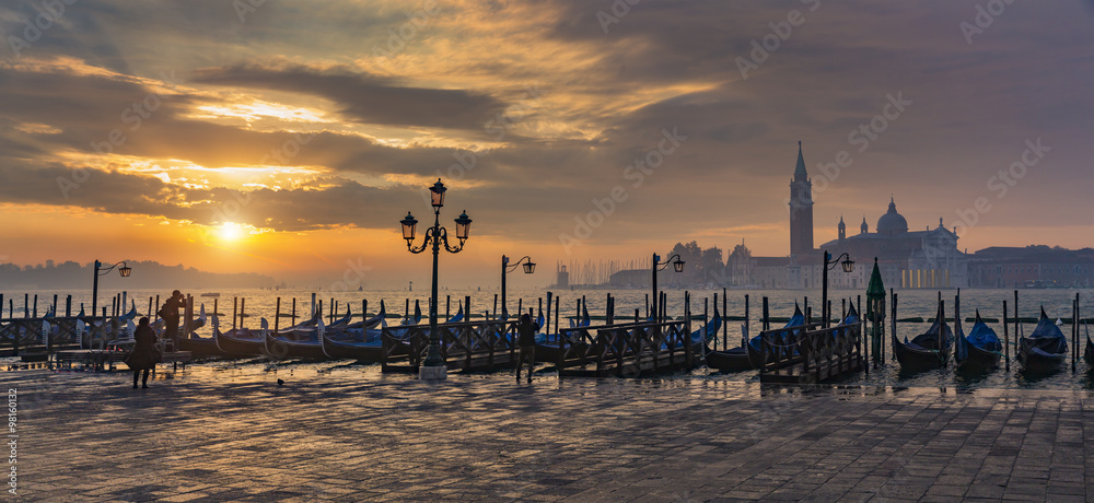 Naklejka premium Gondolas by Saint Mark square during sunrise with San Giorgio di Maggiore church in the background in Venice Italy