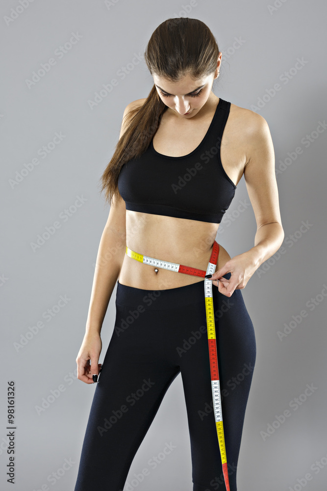 A young woman measuring her waist isolated on gray background