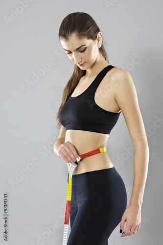 A young woman measuring her waist isolated on gray background © czamfir