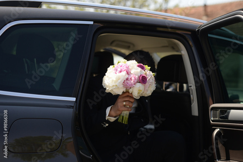 Groom getting out of the car with beautiful bridal bouquet for the bride
