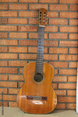 Spanish guitar propped in front of a brick wall as background © rawiii