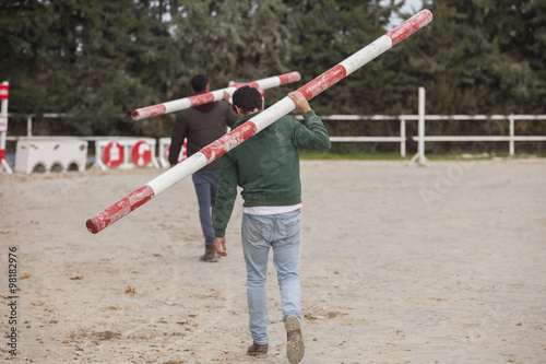 Two assistants loading obstacles poles at horse jumping competit