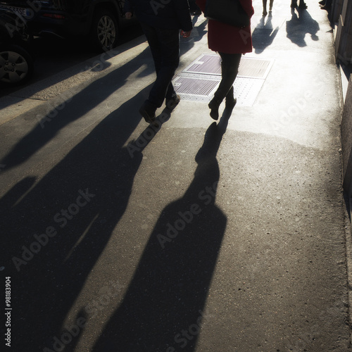 People walking in a busy city district in the late afternoon creating long shadows on the ground