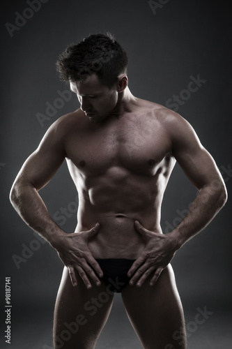 Handsome muscular bodybuilder posing on gray background. Low key studio shot