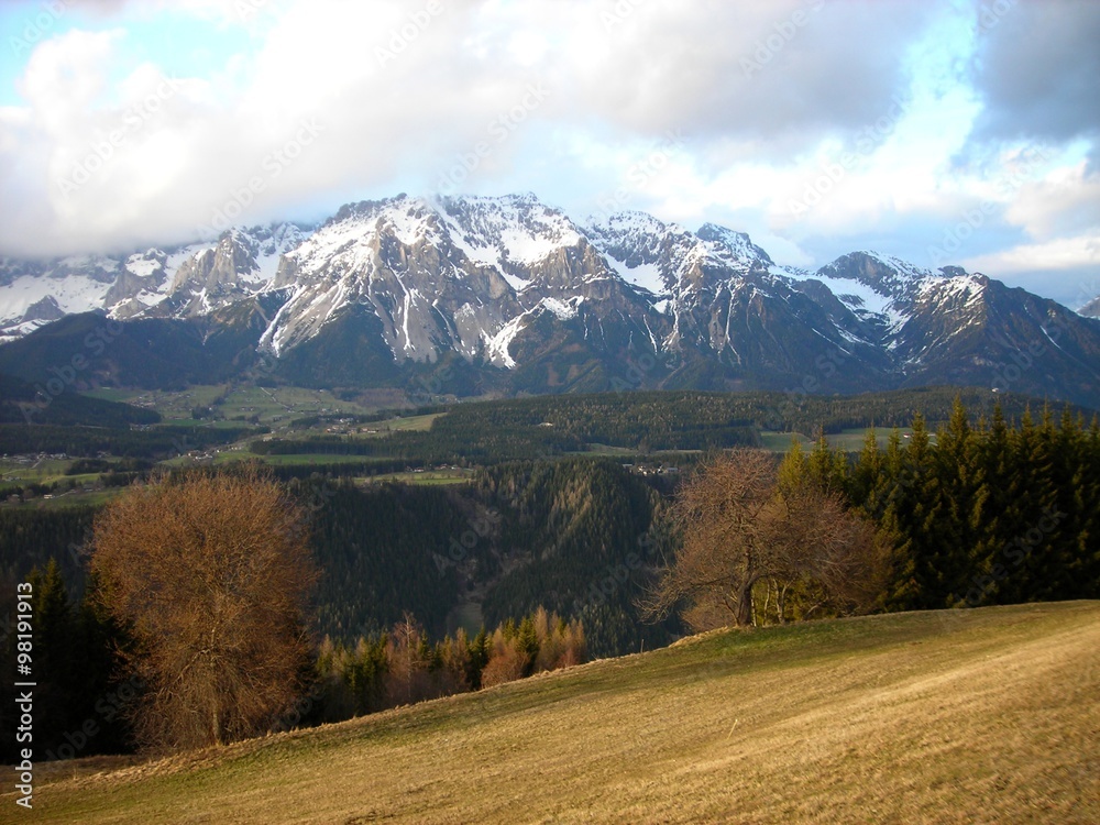 Panoramic view on the early spring landscape in the mountains featuring green hills and snow covered mountain tops in the distance. Austrian Alps, ski resort Schladming.