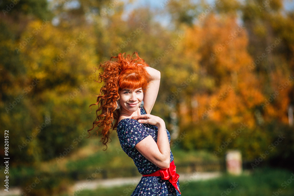 beautiful sexy red-haired girl in a blue dress walks in the autumn park