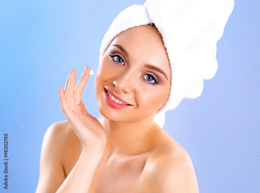Beautiful young woman applying a creme on her face isolated on gray background Beautiful young woman applying a creme on her face isolated on gray background
