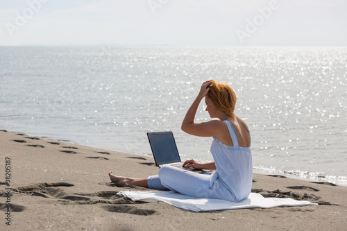 redheaded girl working at a laptop sitting on the beach