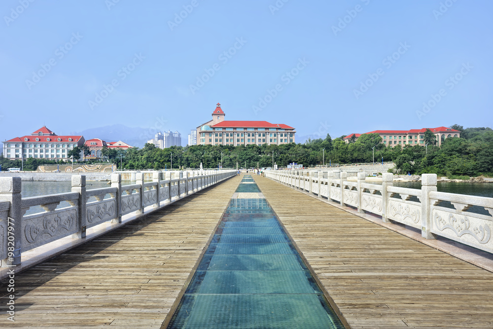 Fototapeta premium Walkway on a pier with stately buildings on the background, Yantai, China