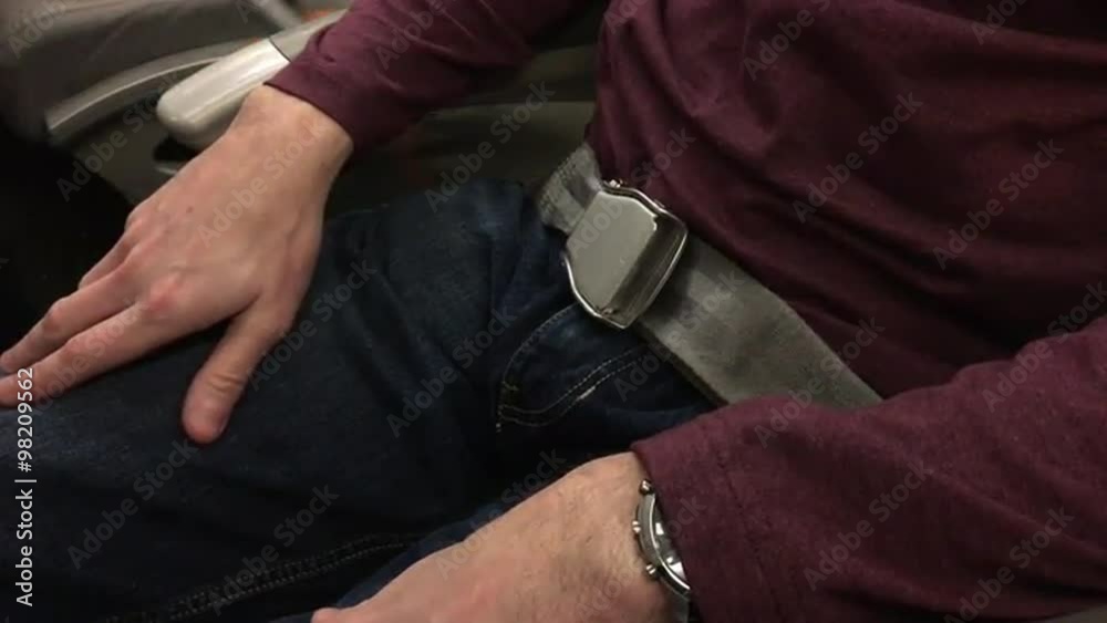 A man fasten his seat belt on an airplane.  	