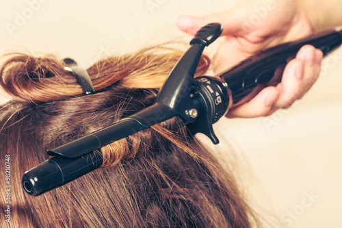 Stylist curling hair for young woman.