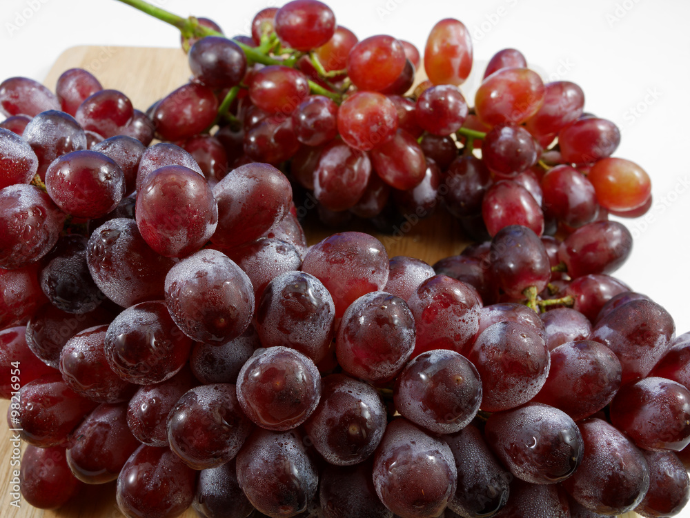 The large bunch of ripe red grapes on the wooden board.