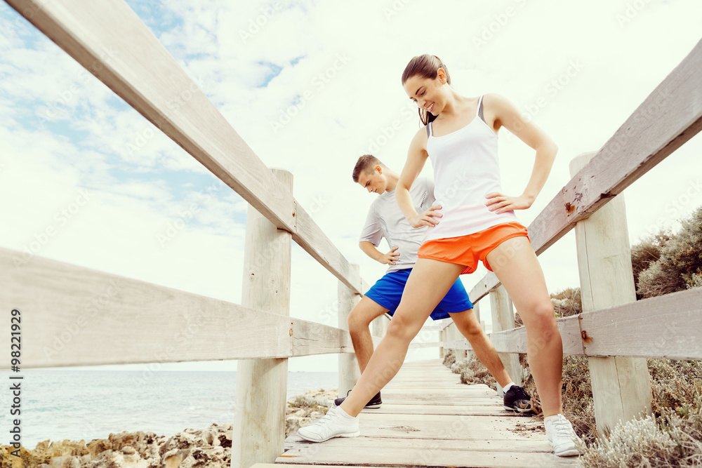 Obraz premium Runners. Young couple exercising and stertching on beach