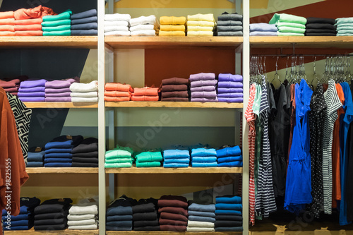 Various color sweatshirts at shelf and shirts on hangers in shop, Italy