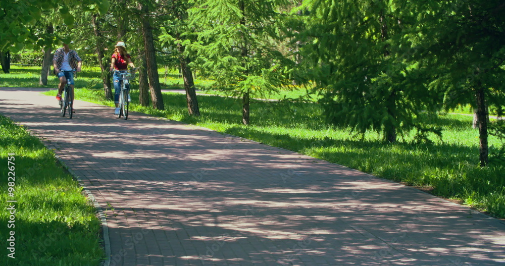 Young couple riding bikes through park on summer day Young couple riding bikes through park on summer day