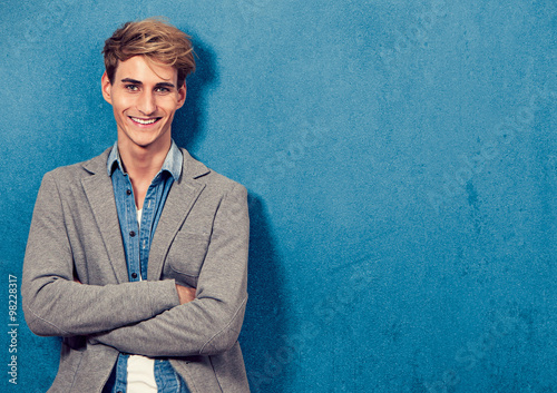 smiling young man leaning beside a blue wall photo