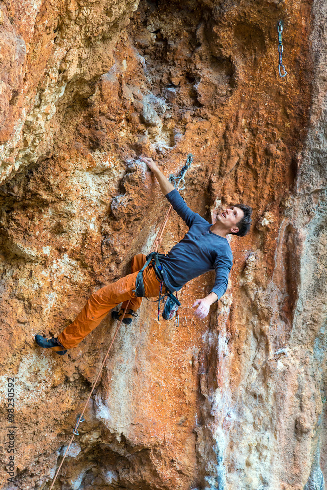 Handsome Climber Hanging on one hand on orange rocky Wall Handsome Climber Hanging on one hand on orange rocky Wall