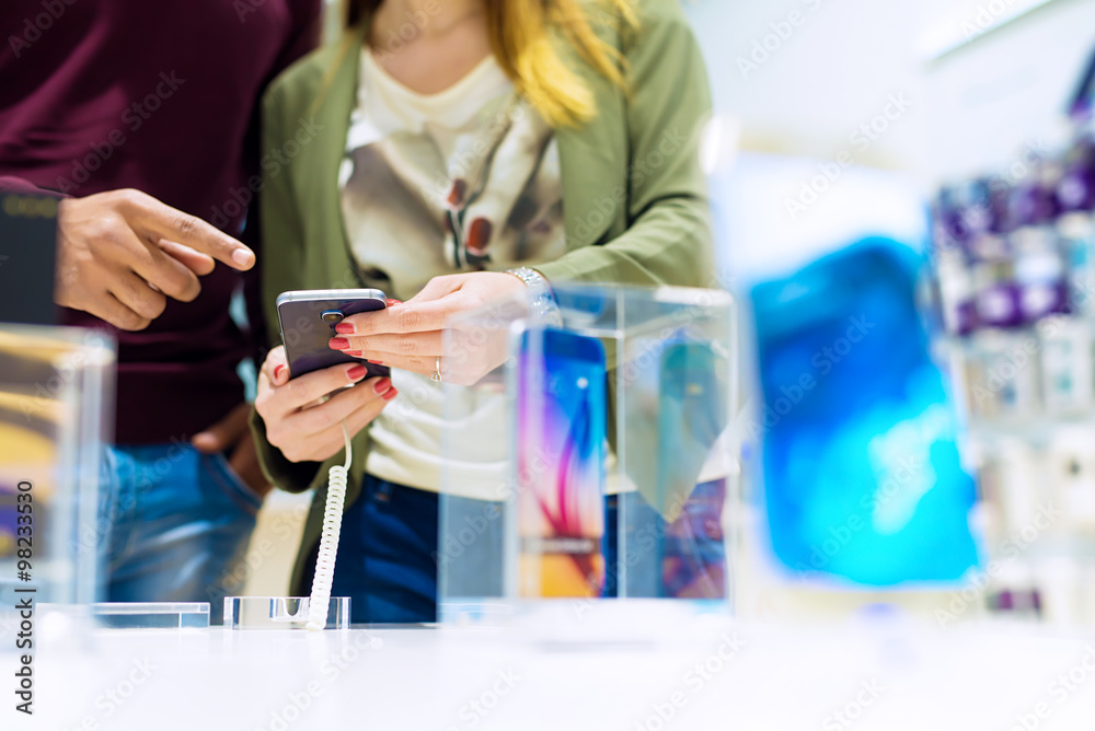Woman holding mobile phone and black man is pointing finger at phone. They are looking for new smart phone. Mobile shop. Shallow depth of field. Woman holding mobile phone and black man is pointing finger at phone. They are looking for new smart phone. Mobile shop. Shallow depth of field.