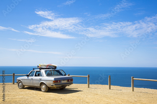 old retro car with surfboards on the roof and ocean in backgroun photo
