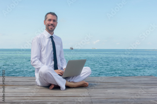 businessman doing yoga on a wooden bridge with a laptop