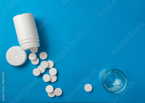 Effervescent pills coming from a white tube on a blue surface, n