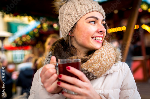 Frau mit Wollmütze genießt warmen Glühwein in der Kälte auf dem Weihnachtsmarkt