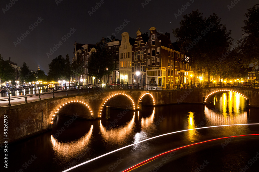 Stripes of light of a tourboat passing by on a canal in Amsterdam at night