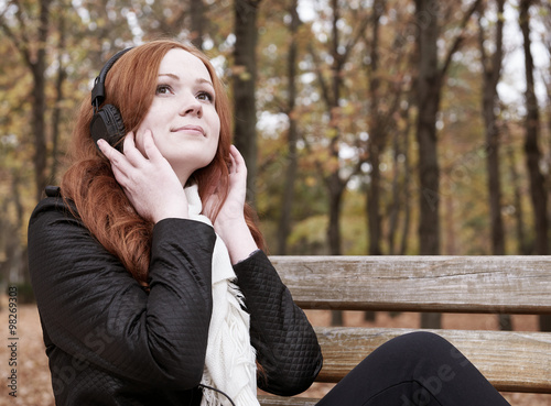 redhead girl with headphones listen music on player in city park, fall season