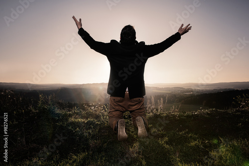 Man with outstretched arms
Rear view of a man with outstretched arms, kneeling in the grass on top of a hill.