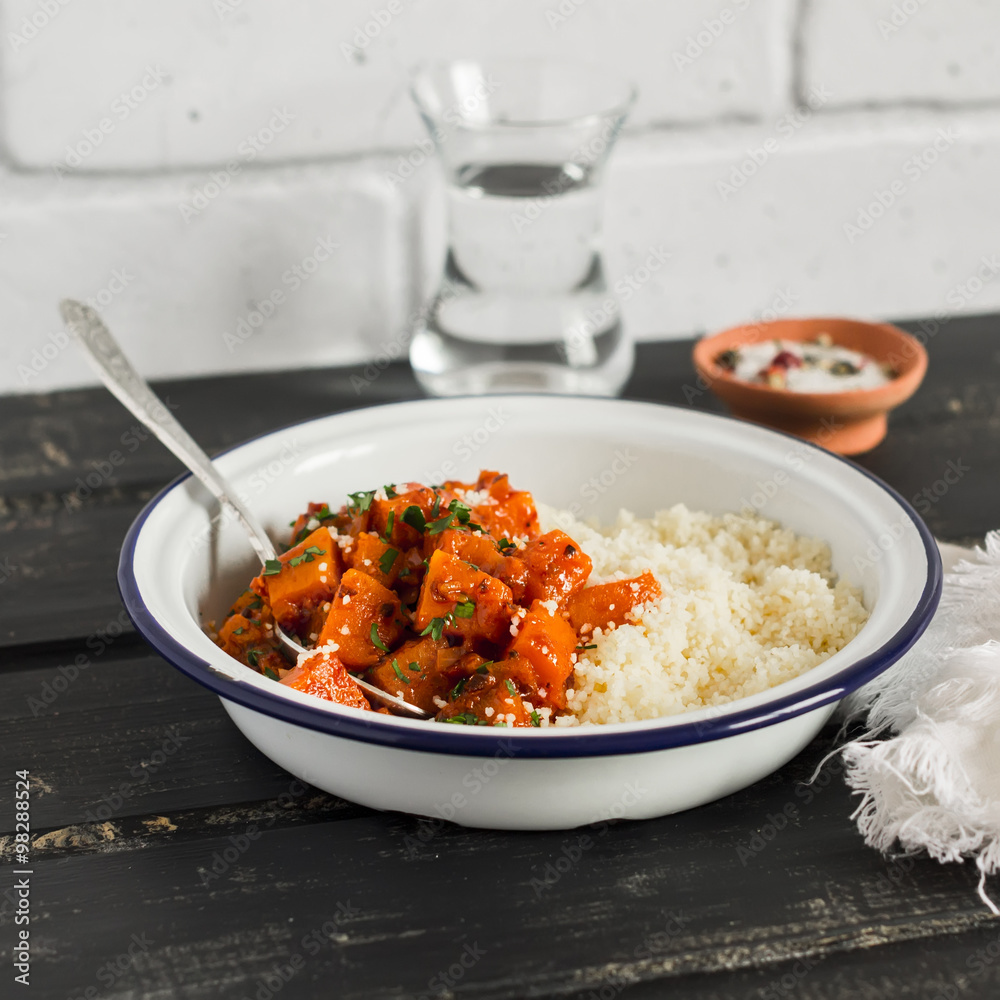 Healthy food - pumpkin stew and couscous in a white enamel bowl on a dark wooden Board. A vegetarian lunch. Rustic style