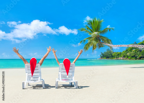 Couple in Santa hats on sun beds at palm beach © EMrpize