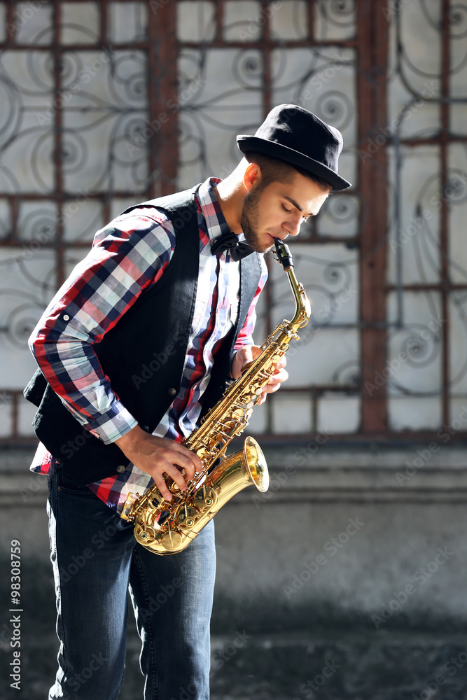 Naklejka premium Young man plays saxophone on urban background