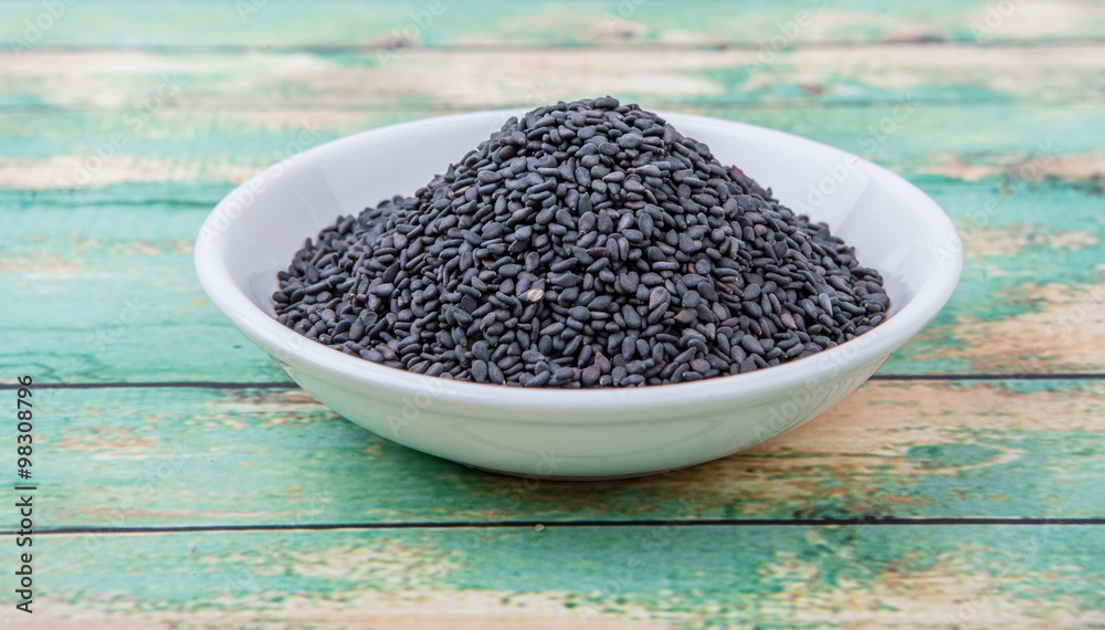 Black sesame seed in white bowl over wooden background Black sesame seed in white bowl over wooden background